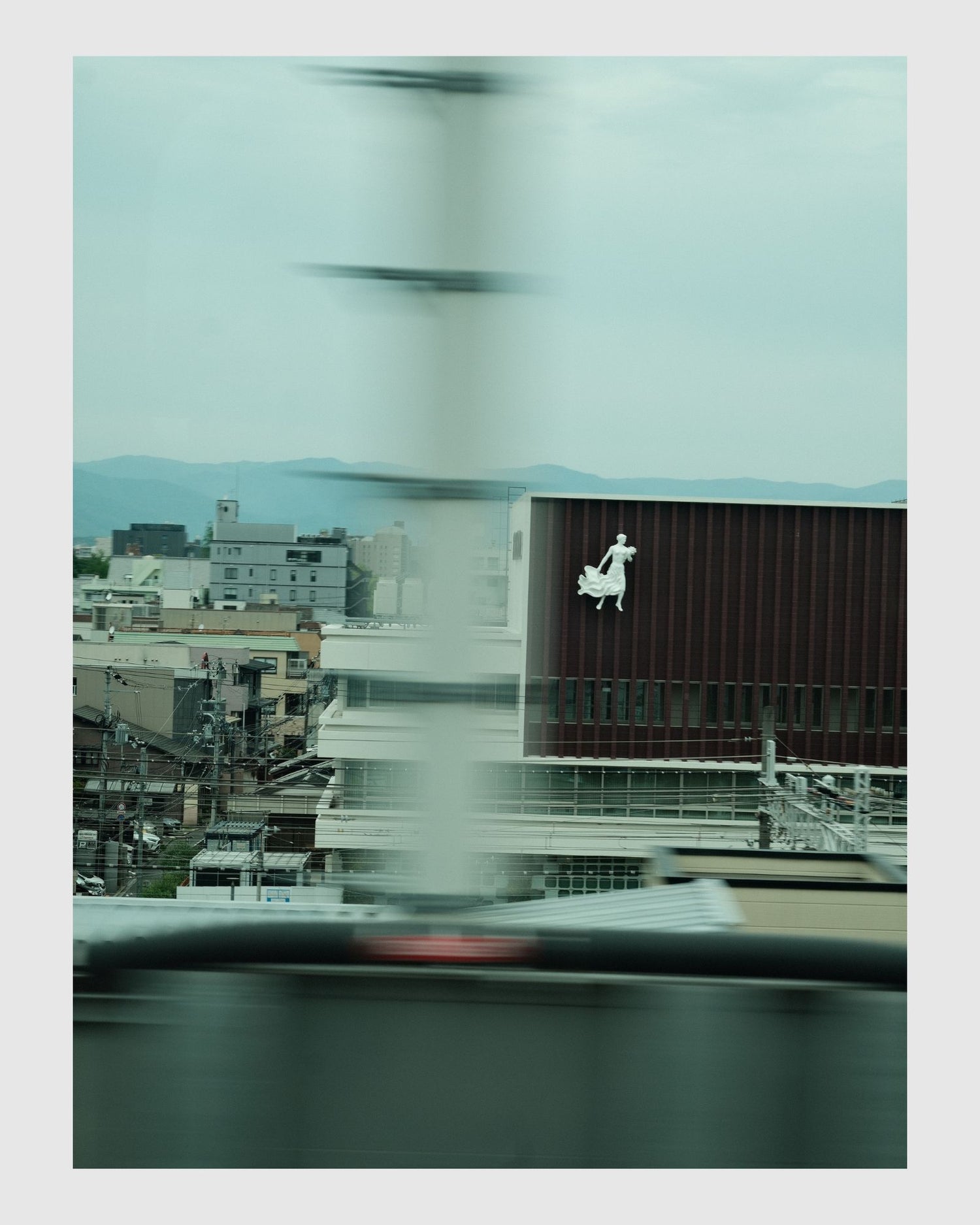 Cityscape view from a vehicle window with blurred motion, featuring a building with a logo.