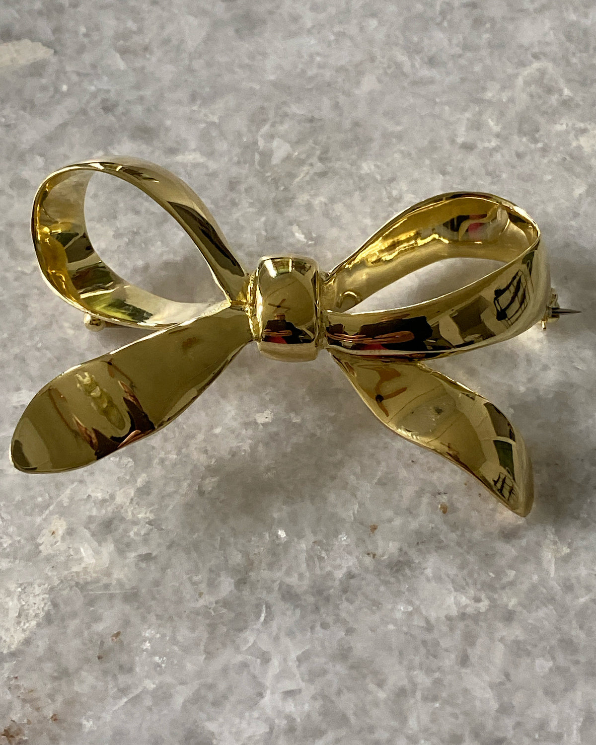 A gold solid bow brooch sits on marble