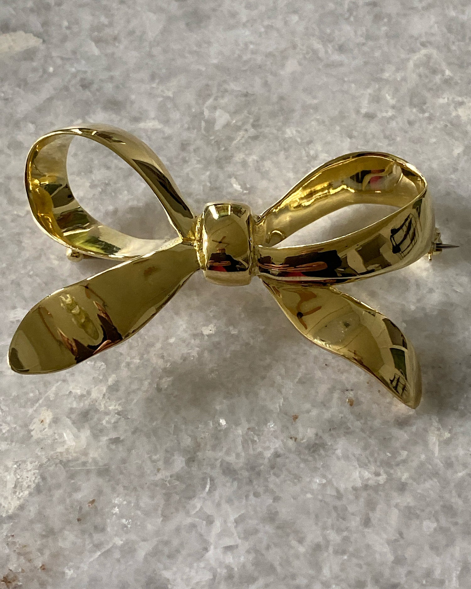 A gold solid bow brooch sits on marble