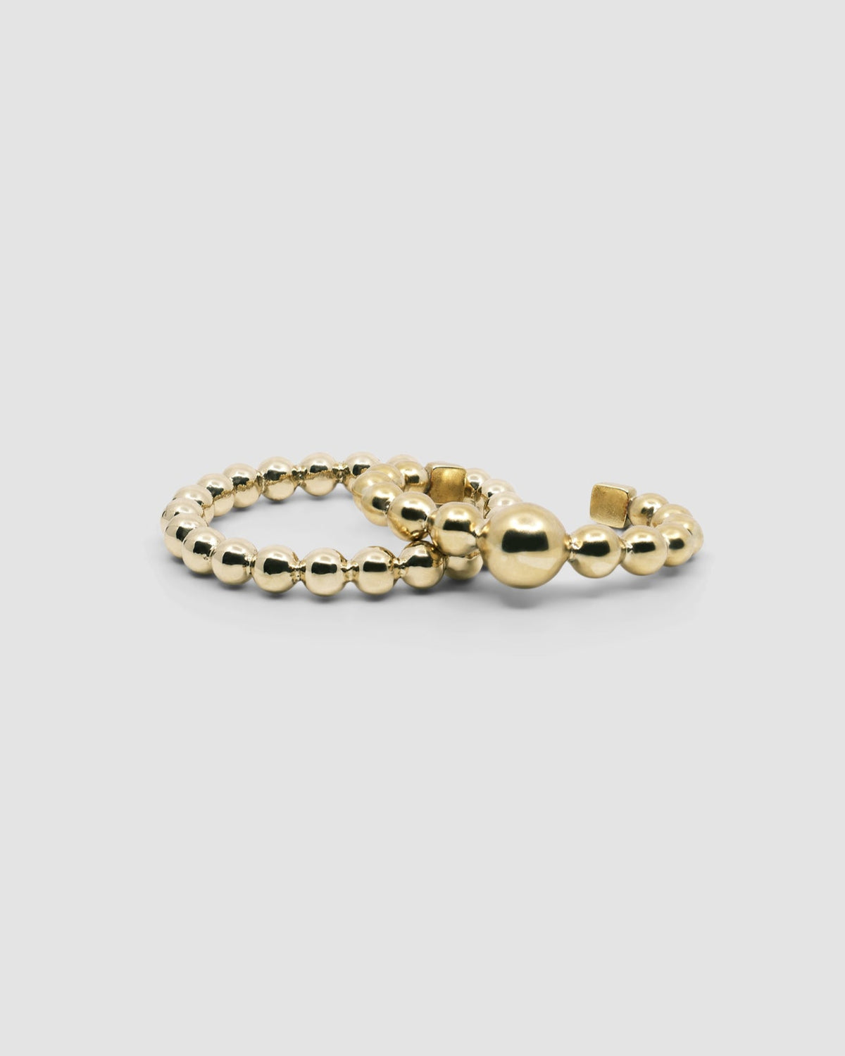 an open gold cuff bangle consisting of numerous interlinked gold balls sits with a ball gold bangle