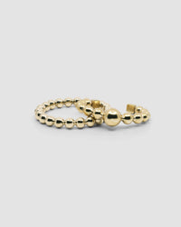 an open gold cuff bangle consisting of numerous interlinked gold balls sits with a ball gold bangle