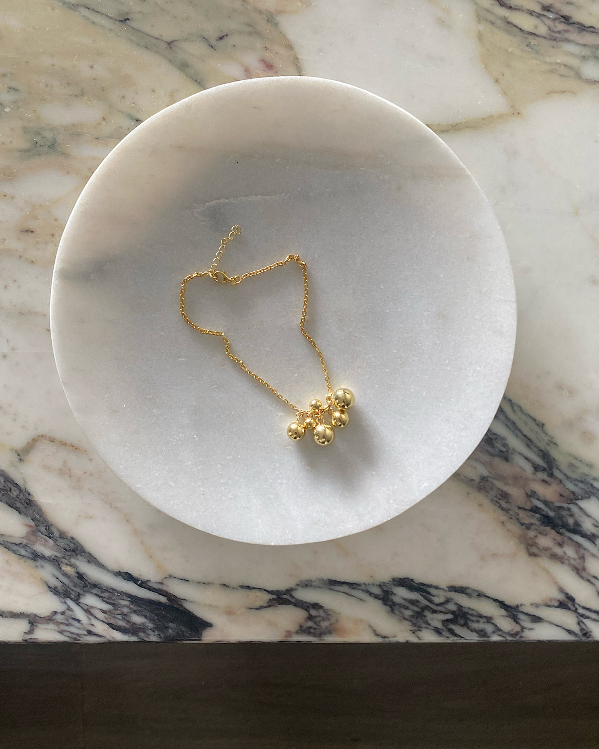 A gold anklet sits on a white marble plate. Anklets from the Pared Store, Sydney