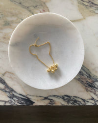 A gold anklet sits on a white marble plate. Anklets from the Pared Store, Sydney