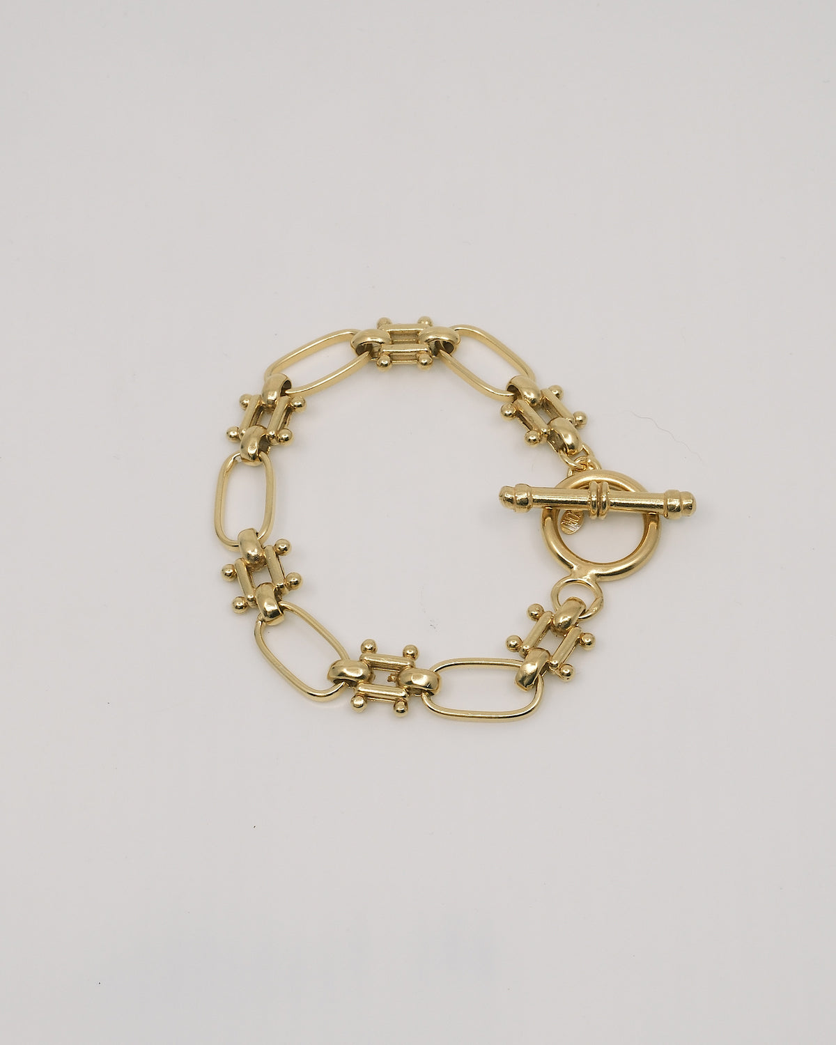 an unusal fob link bracelet in gold sits on a grey background