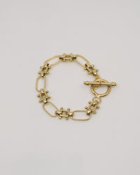 an unusal fob link bracelet in gold sits on a grey background