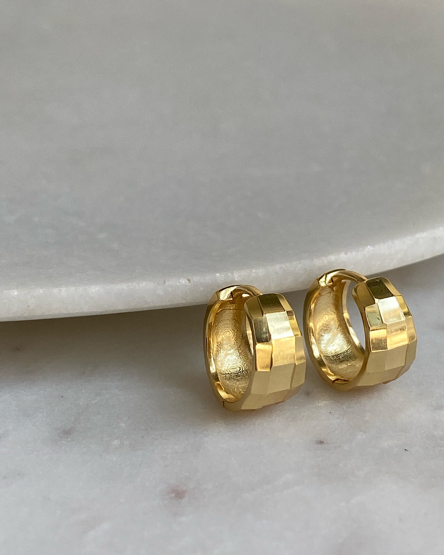 A pair of gold-plated sterling silver hinged huggie hoop earrings with a facetted texture, displayed on a white surface.