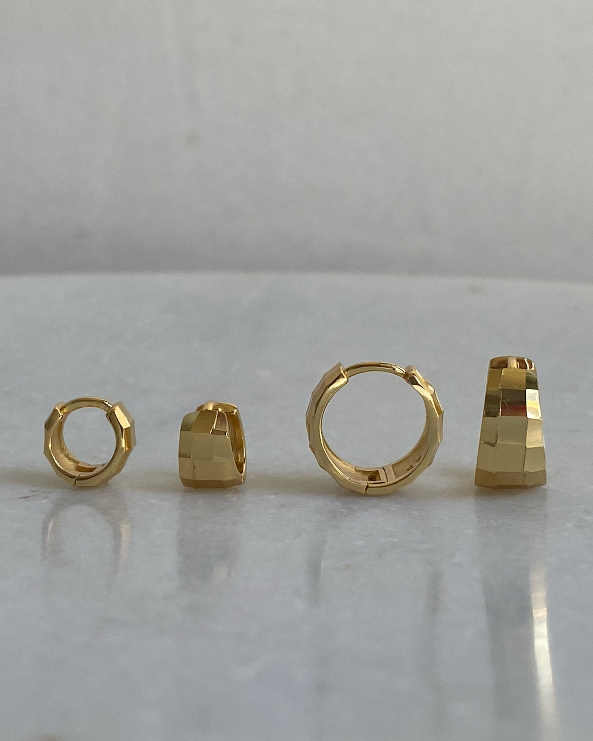 A pair of gold-colored hoop earrings with a textured faceted design, displayed on a white background.