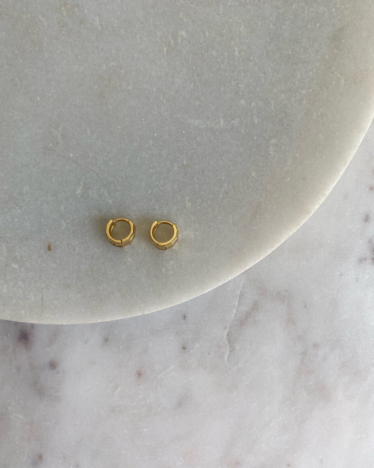 A pair of gold-plated sterling silver hinged huggie hoop earrings with a facetted texture, displayed on a white surface.