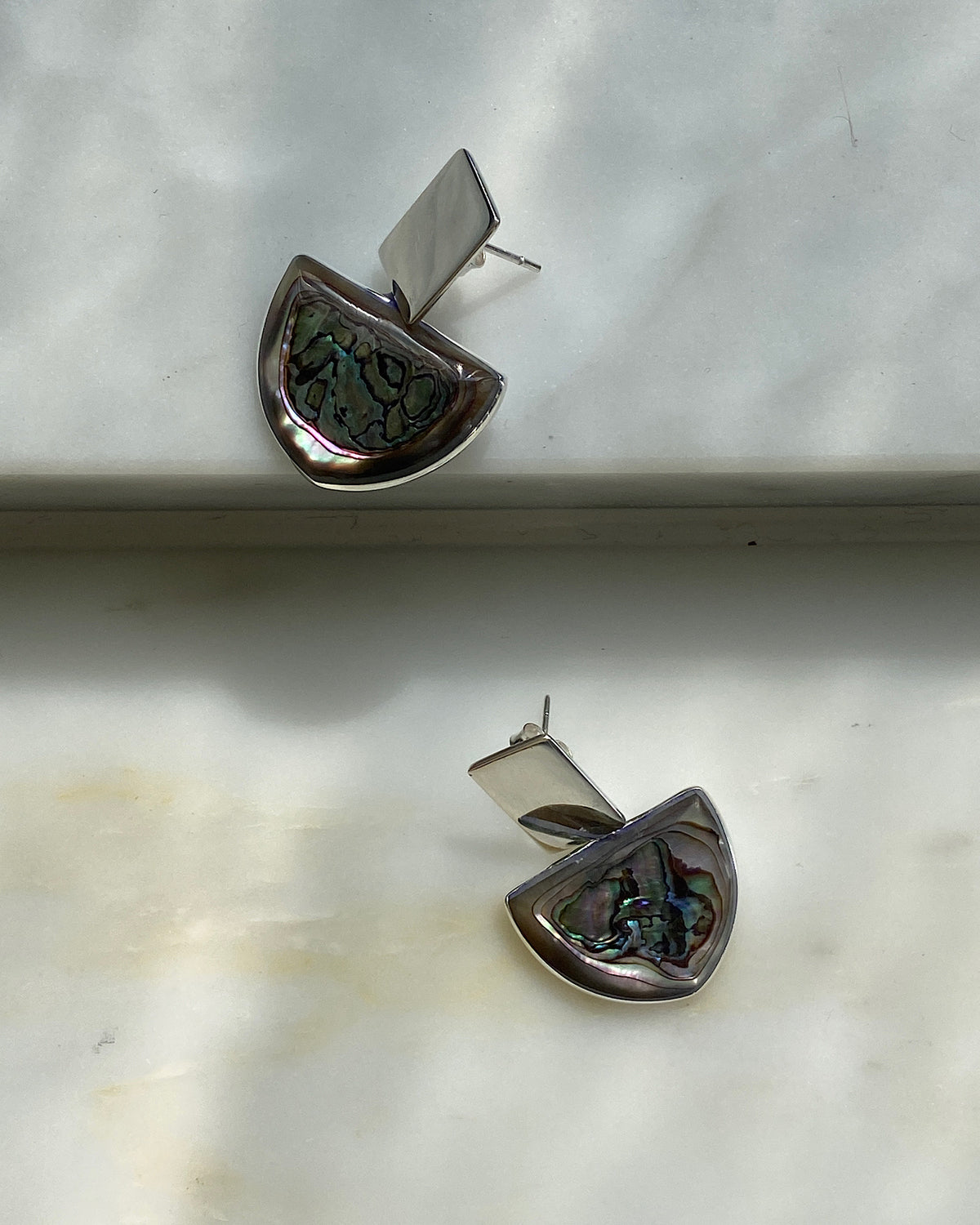 Silver rectangle said top earrings with a half circle of abalone hanging off sit on a marble base from Surry Hills Studio The Pared Store