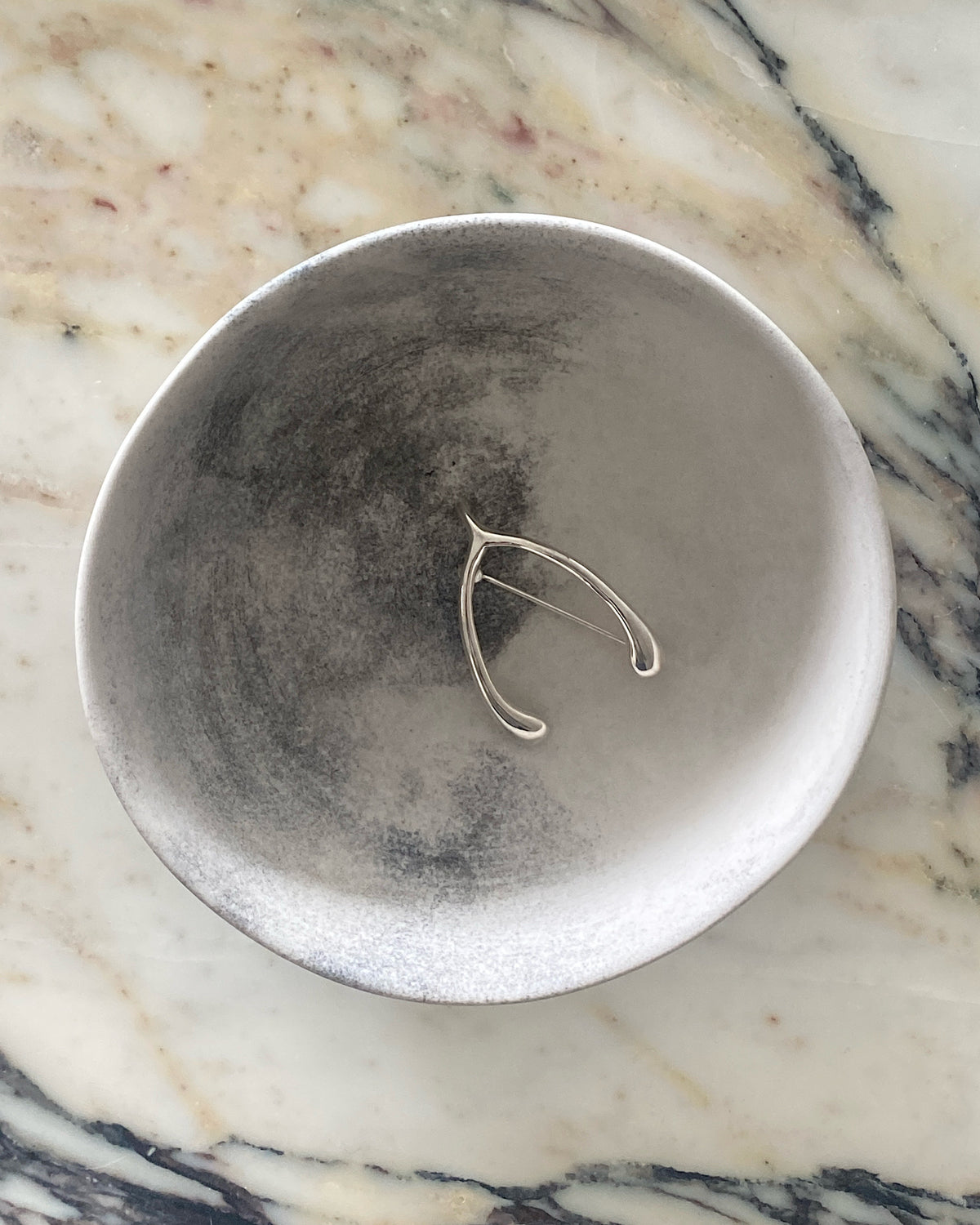 Silver wishbone brooch sits in a bowl. Available at The Pared Store, Surry Hills