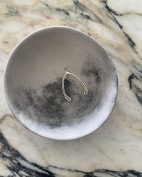 A silver brooch in the shape of a wishbone sits in a biwl on a marble top