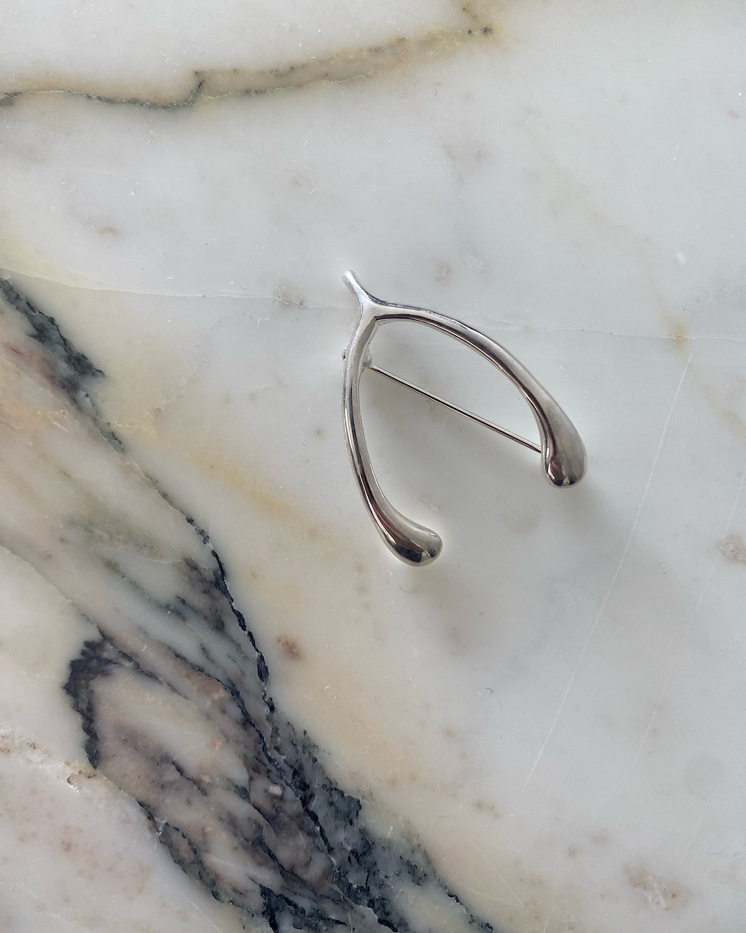 sterling silver wishbone brooch sits on a marble background. Silver brooches at The pared Store