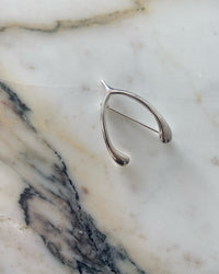sterling silver wishbone brooch sits on a marble background. Silver brooches at The pared Store