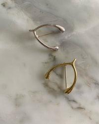 a gold and a silver wishbone brooch sit on a marble base