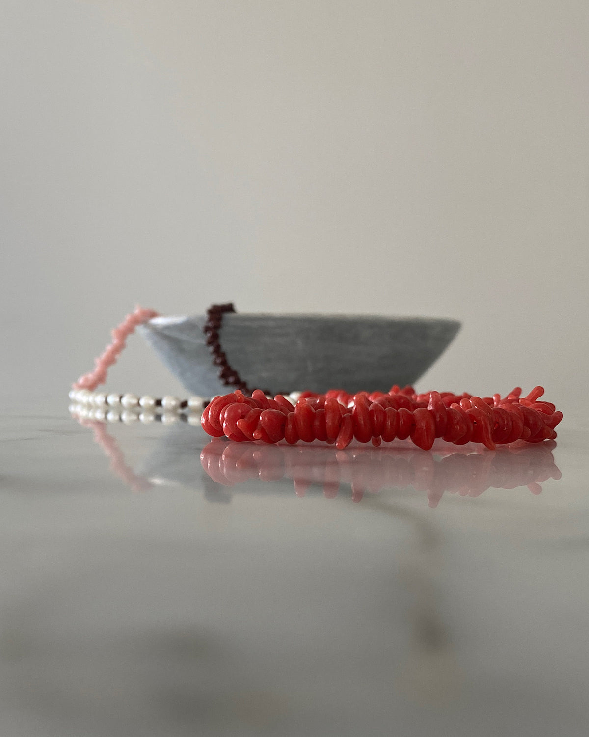 Red, pink, chocolate glass bead necklace with cream pearls sit in a bowl on marble