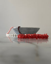 Red, pink, chocolate glass bead necklace with cream pearls sit in a bowl on marble