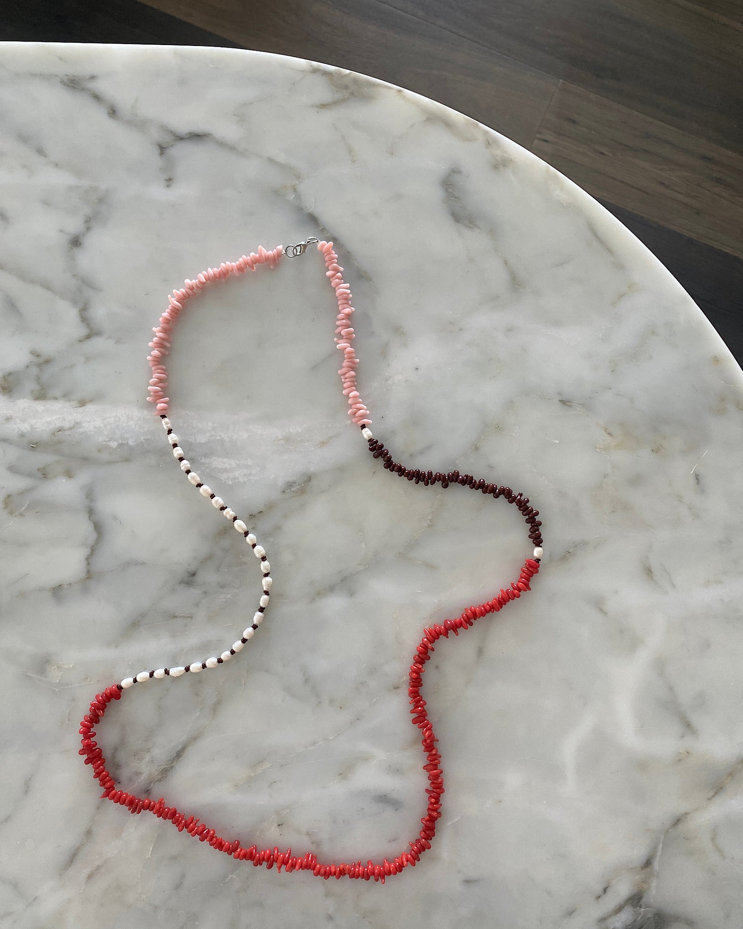 Red, pink, chocolate glass bead necklace with cream pearls sit in a bowl on marble