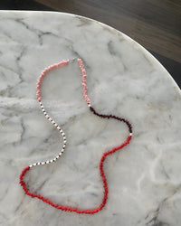 Red, pink, chocolate glass bead necklace with cream pearls sit in a bowl on marble