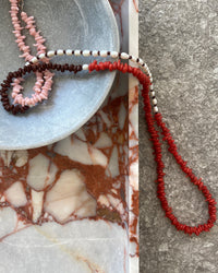 Red, pink, chocolate glass bead necklace with cream pearls sit in a bowl on marble