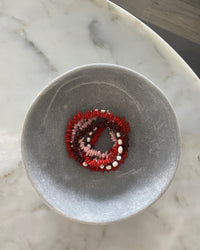 Red, pink, chocolate glass bead necklace with cream pearls sit in a bowl on marble