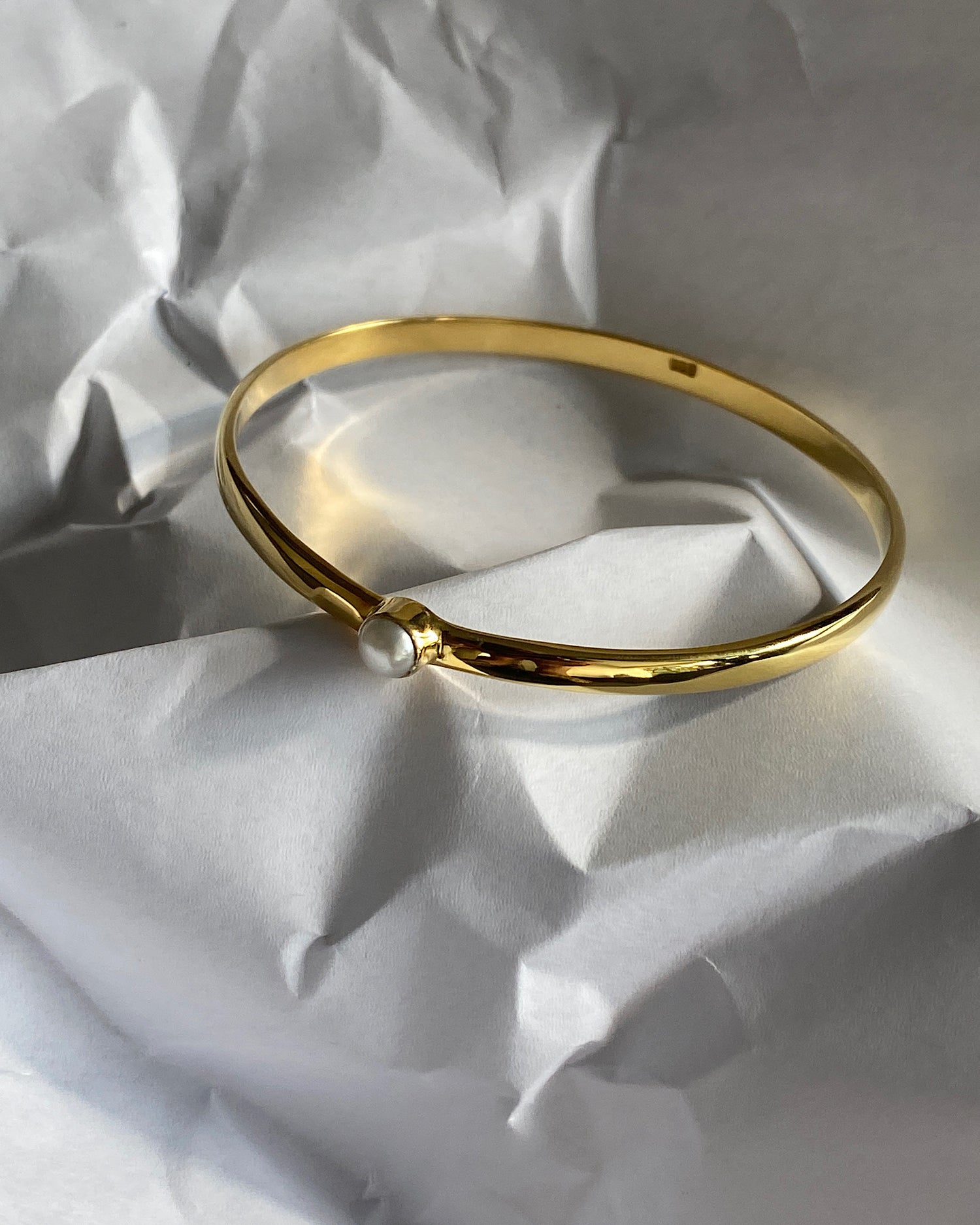 simple thin gold bangle with a single pearl inlaid half way around it