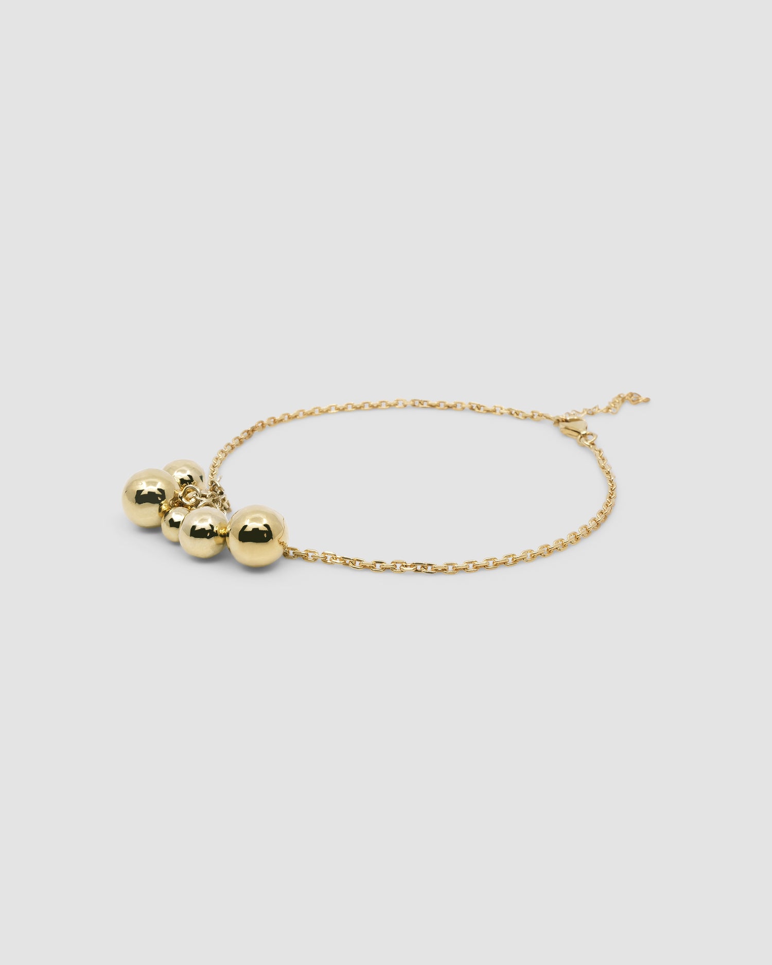A gold anklet with gold balls sits on a grey background