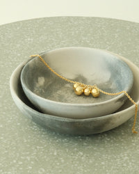 A gold anklet with gold balls sits in a bowl on a table. Available from the parec Store, Sydney