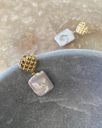 gold quilted studs with rectangular pearls hanging from them sit in a bowl