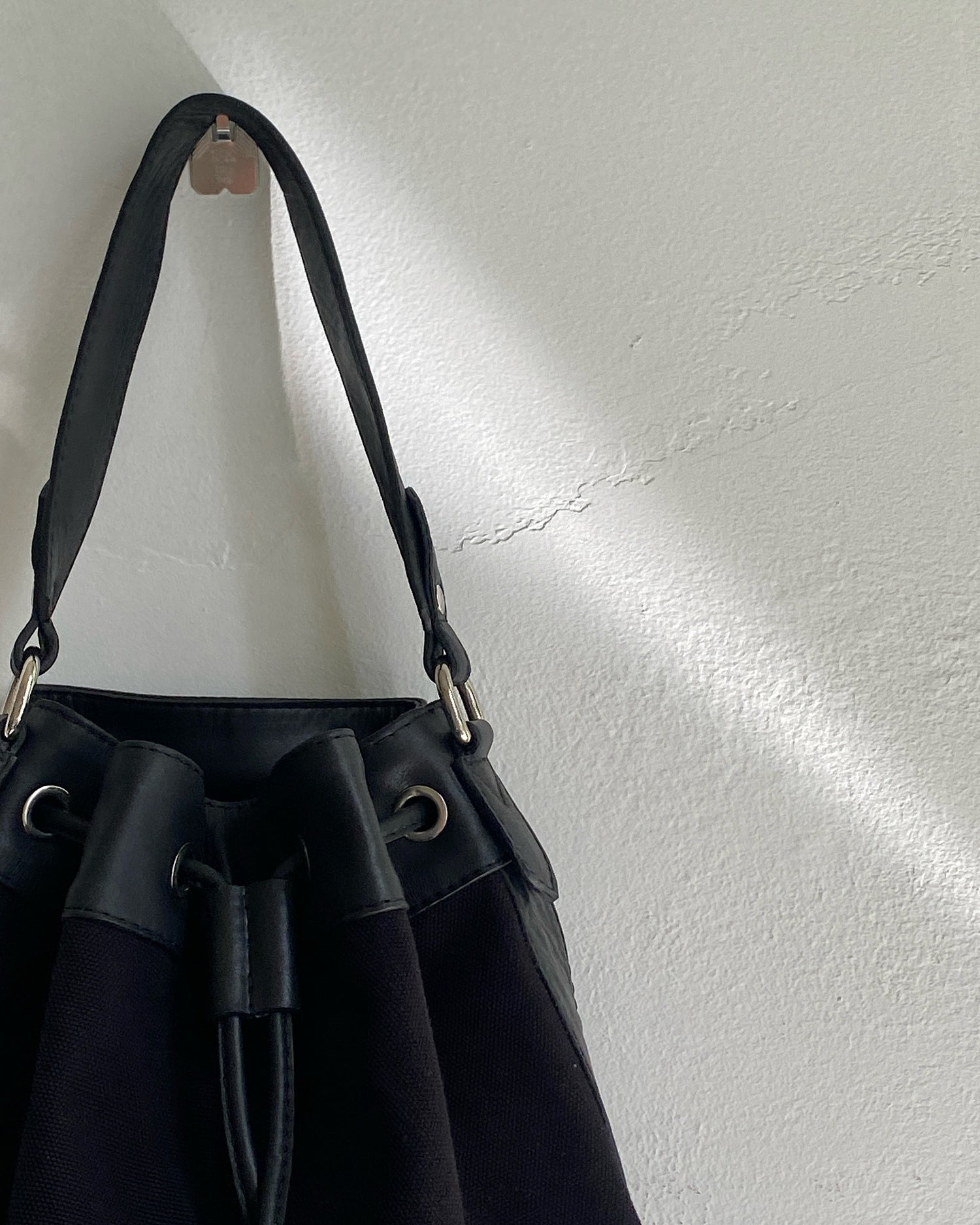 A black canvas bucket bag sits on a wall The Pared Store