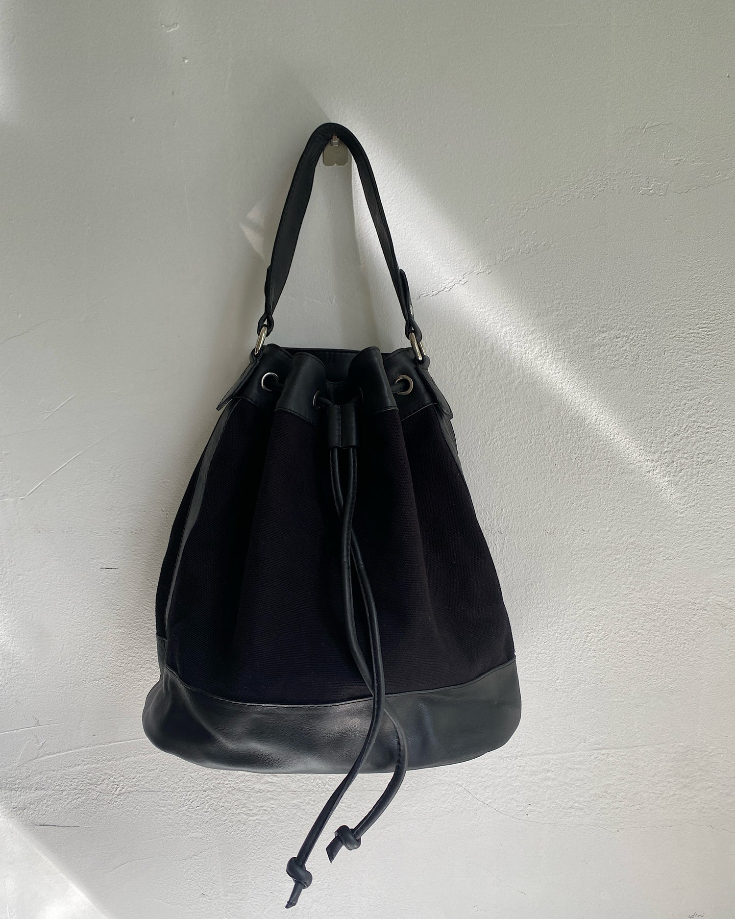 A black canvas bucket bag sits on a wall The Pared Store