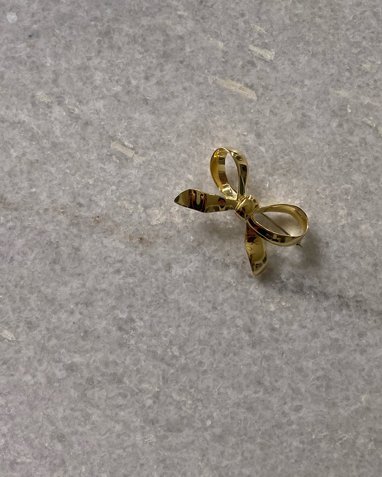A gold solid bow brooch sits on marble