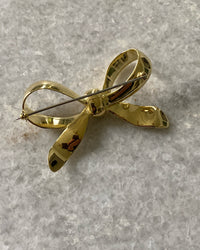 A gold solid bow brooch sits on marble, shown from behind