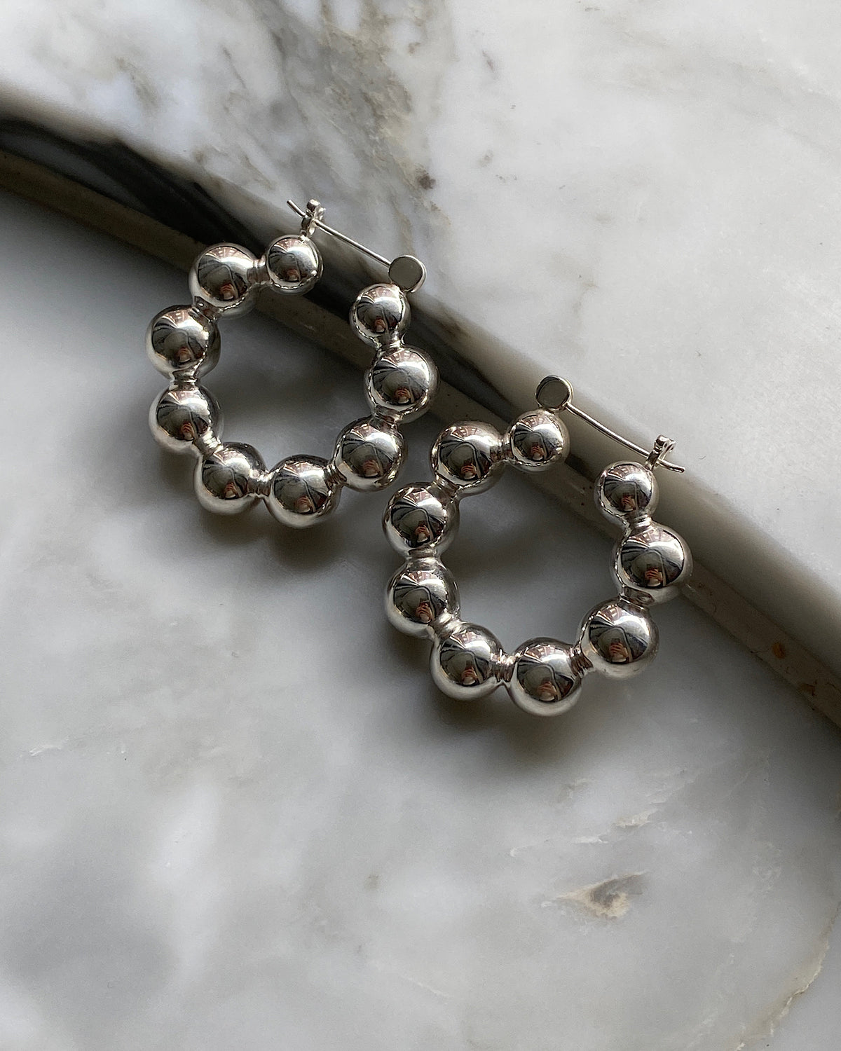 silver hoop earrings made from a serious a balls sit against a marble background