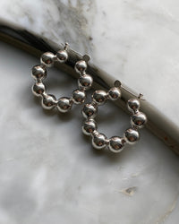 silver hoop earrings made from a serious a balls sit against a marble background