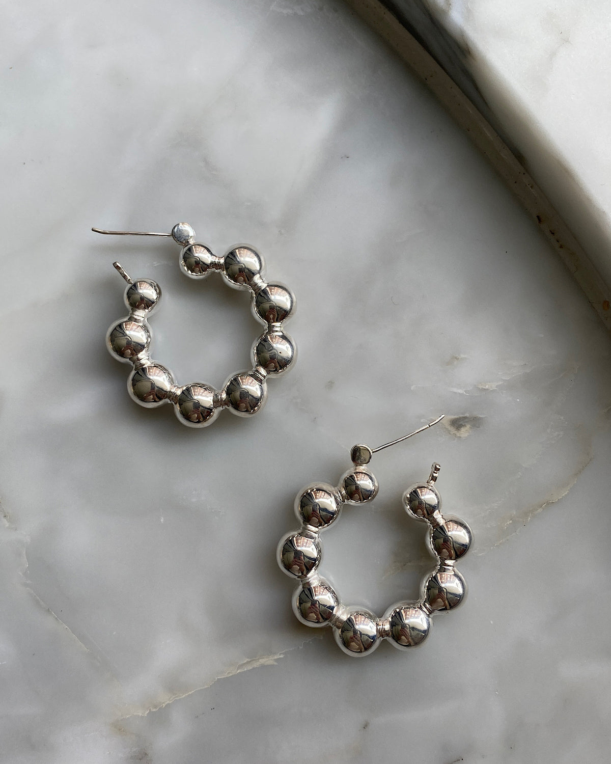silver hoop earrings made from a serious a balls sit against a marble background