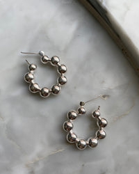 silver hoop earrings made from a serious a balls sit against a marble background