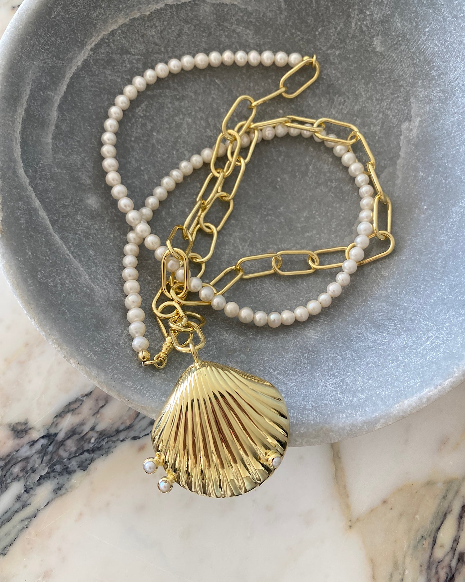 A gold shell pendant with pearls sit on a pearl & chain wrap style necklace