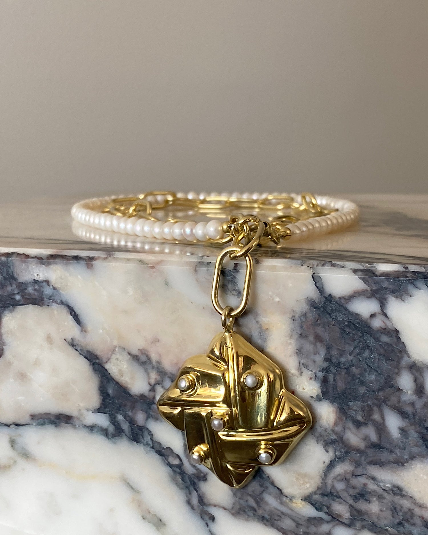 a vintage square gold woven pendant with pearls sits on a gold and pearl wrap style necklace