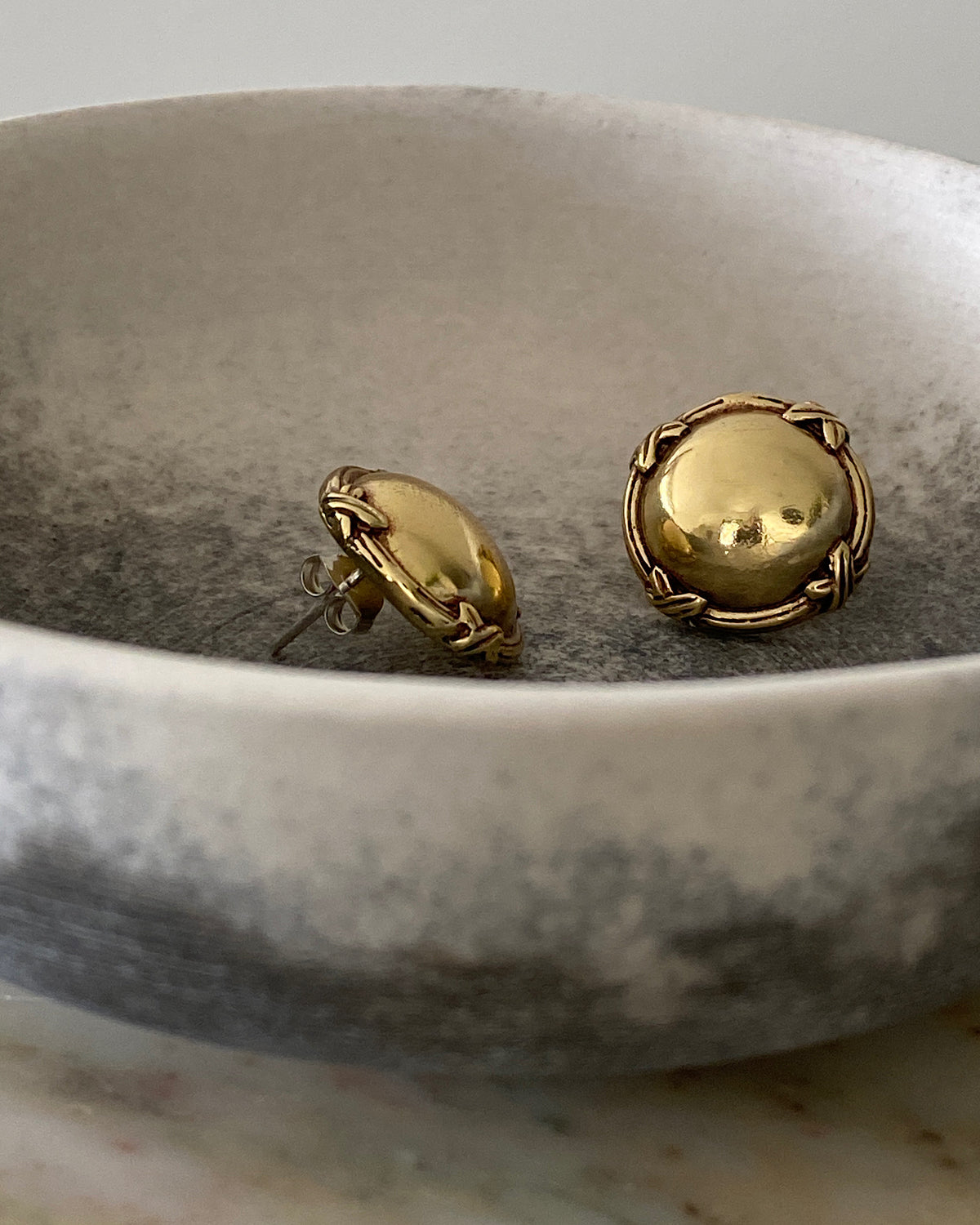 gold round flat earrings with an edge  details sit in a bowl