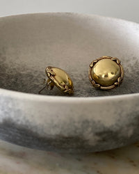 gold round flat earrings with an edge  details sit in a bowl