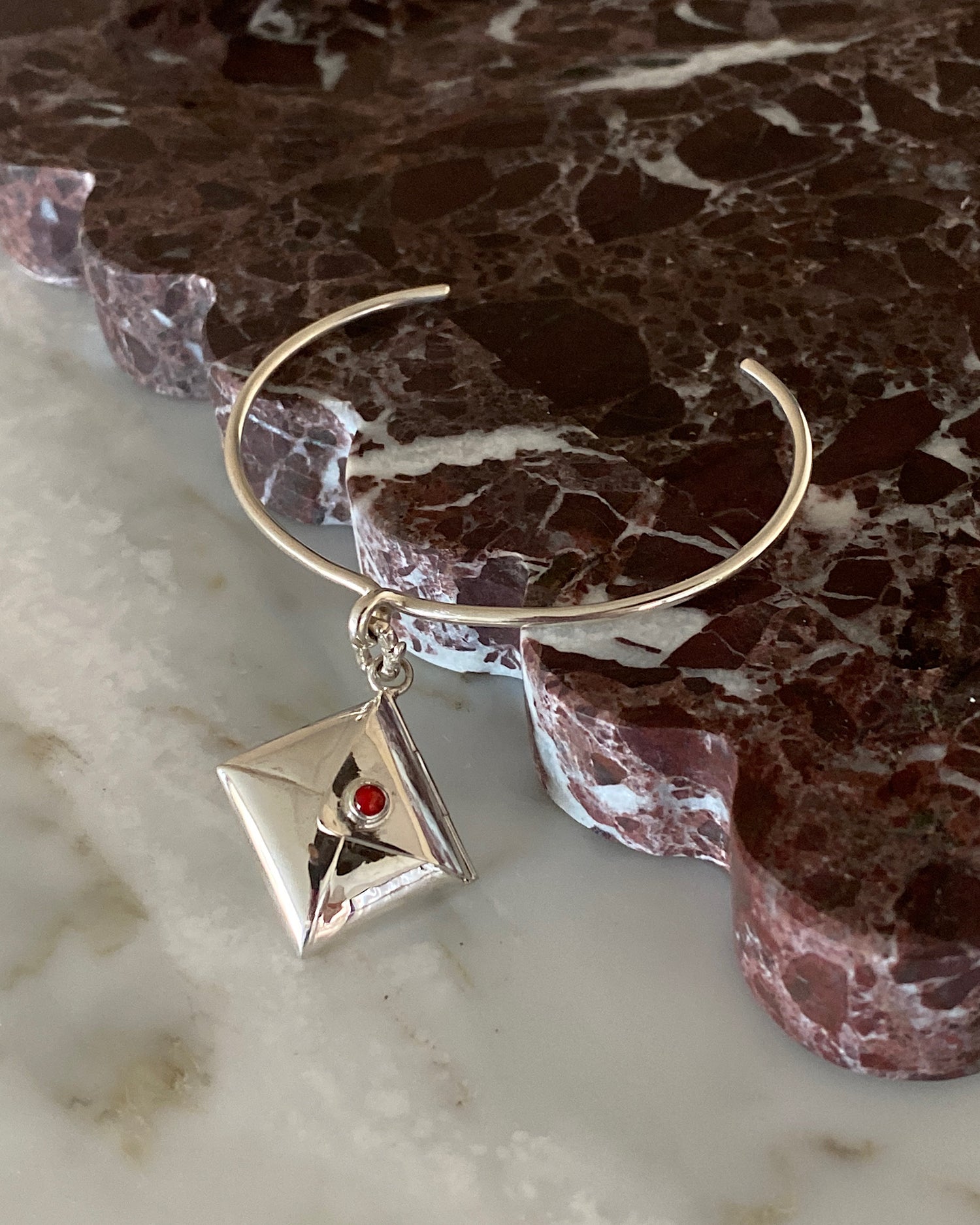 thin open silver cuff with a central loop with a charm attached