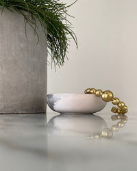 an open gold cuff bangle consisting of numerous interlinked gold balls sits in a bowl