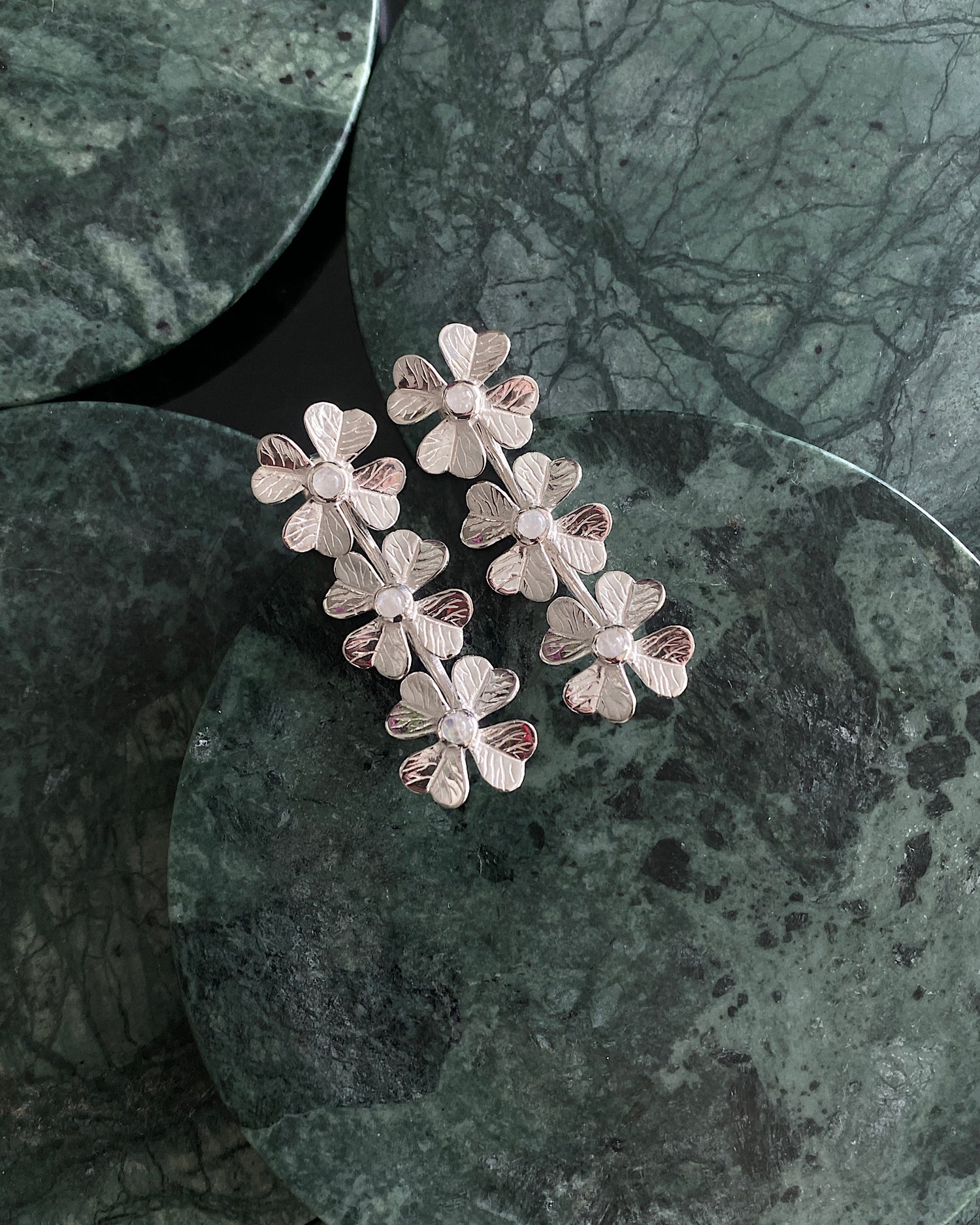 Silver flower & moonstone drop earrings rest on green marble