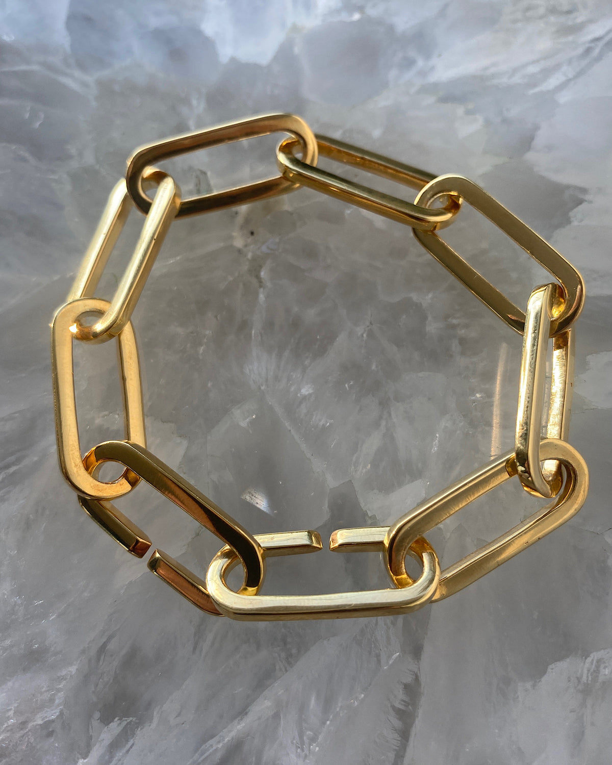 gold curved chain bracelet sits on a stone board