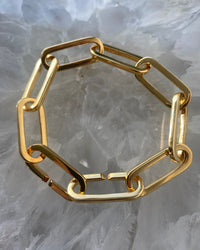 gold curved chain bracelet sits on a stone board