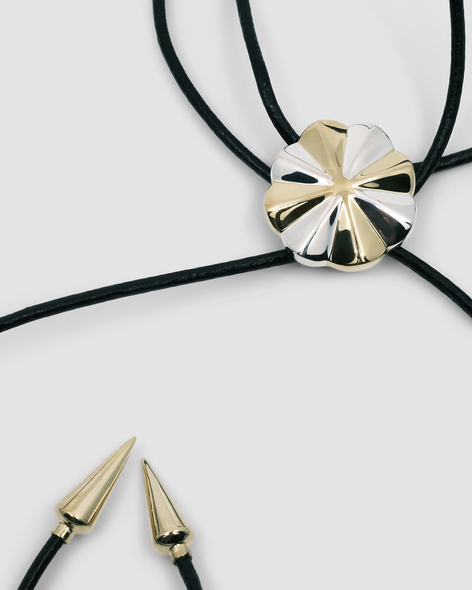 silver & gold pinwheel shaped pendant sits on a leather lariat