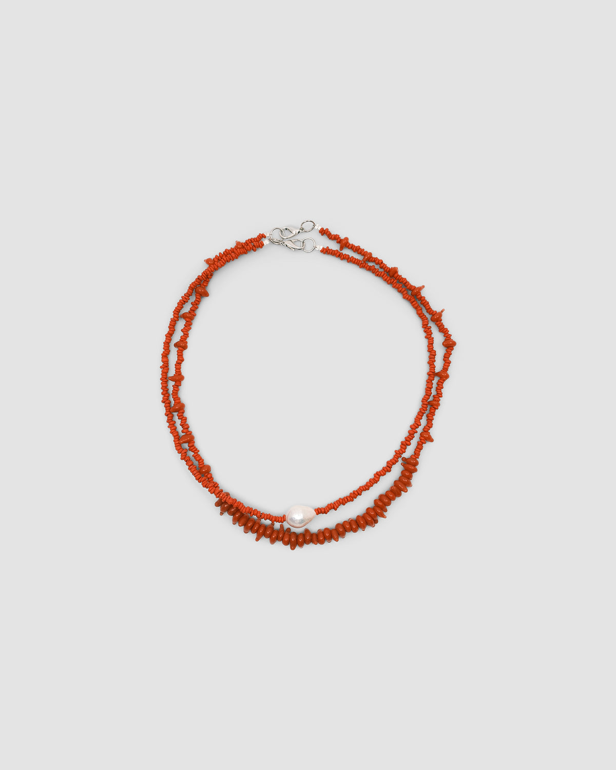 a single baroque pearl floats on a red bead necklace