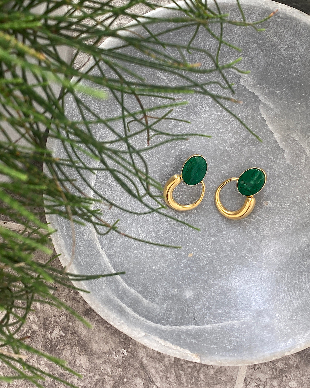 Green stone studs earrings with gold irregular hoops hanging off the bottom in a stone bowl
