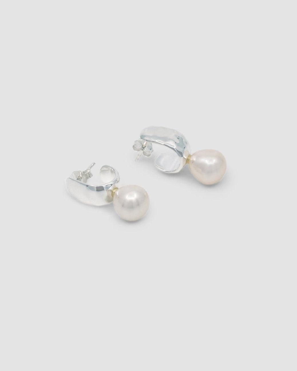 Small silver wide beaten hoop earrings featuring a suspended pearl
