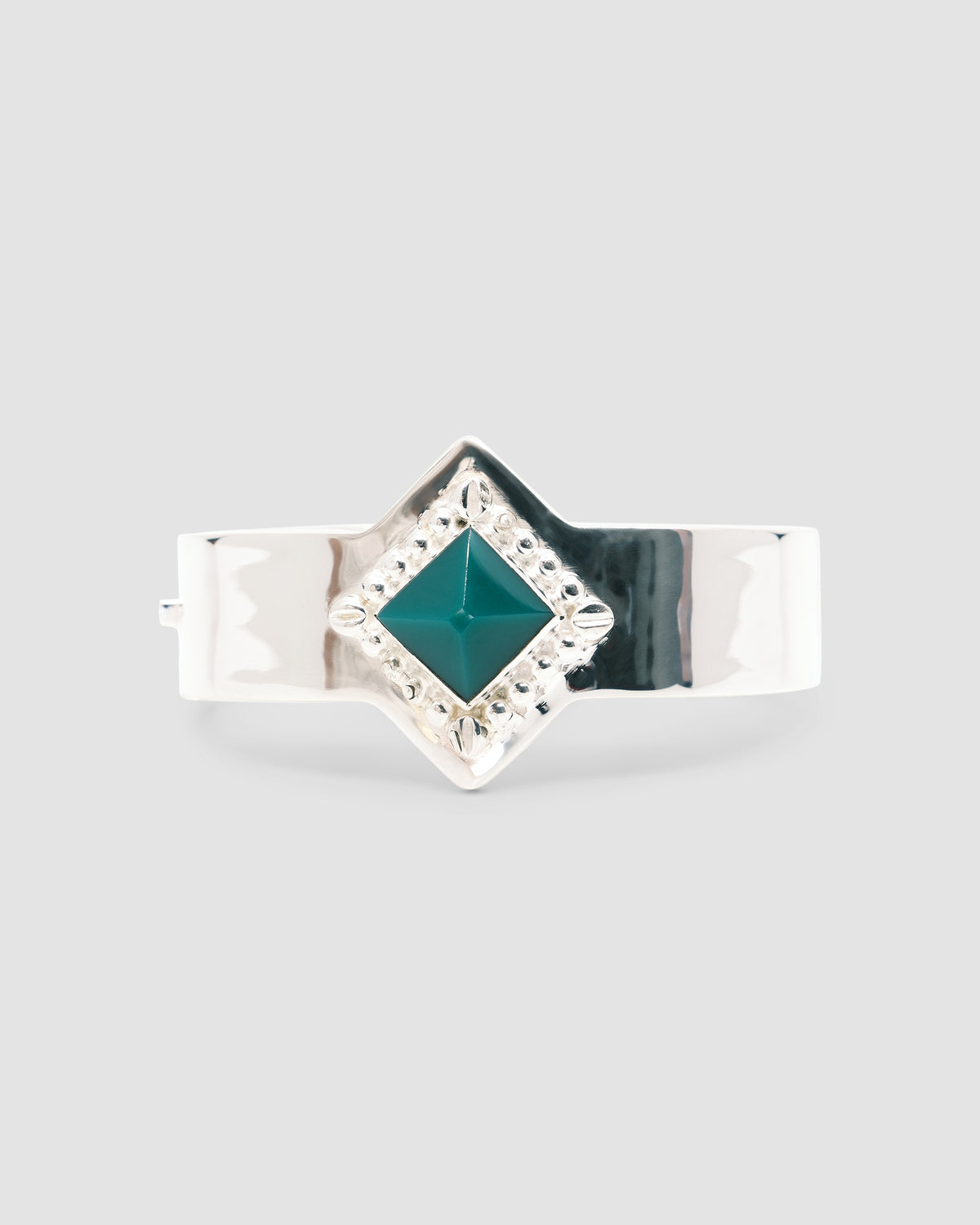 a silver cuff bracelet with a green sqaure stone set into it and beading around the exterior